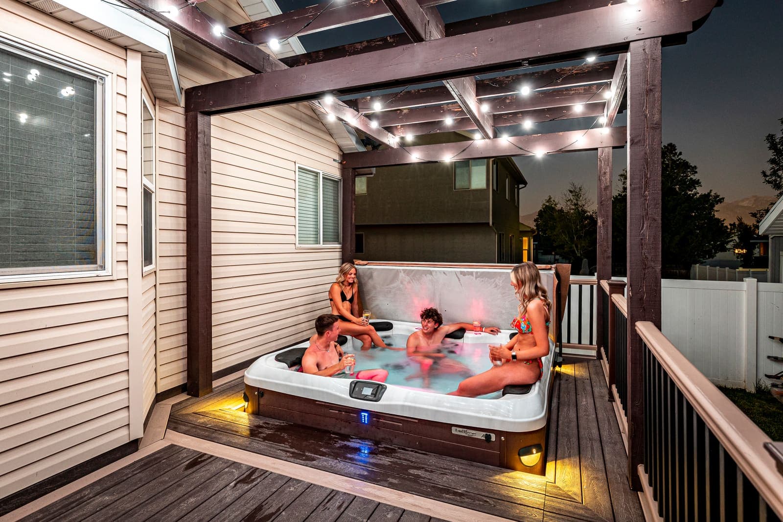 A hot tub under a pergola strung with globe lighting.