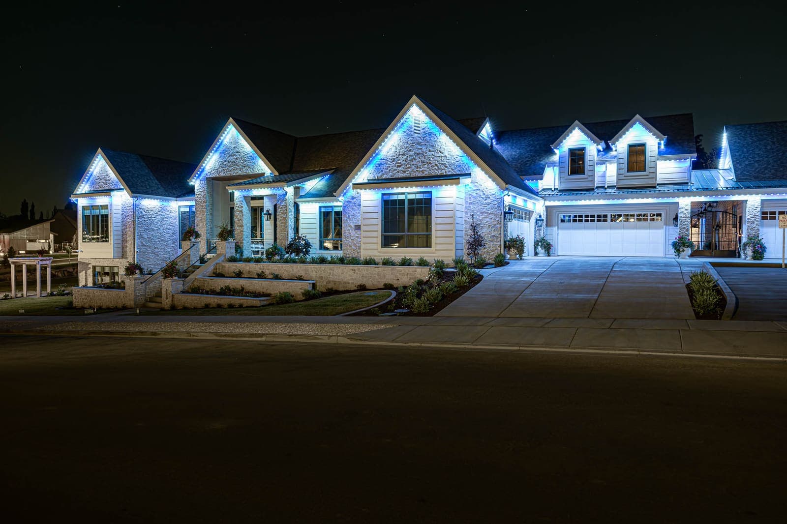 A home's gables and roofline illuminated in white permanent lighting beneath a deep blue evening sky.