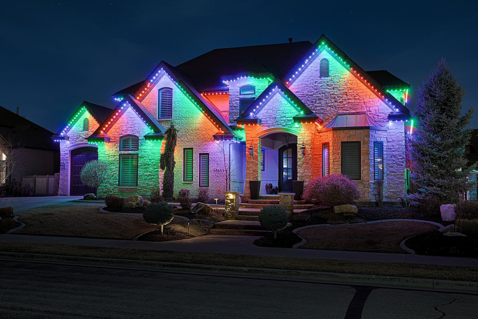A stone entry with trees and plantings uplit in color.