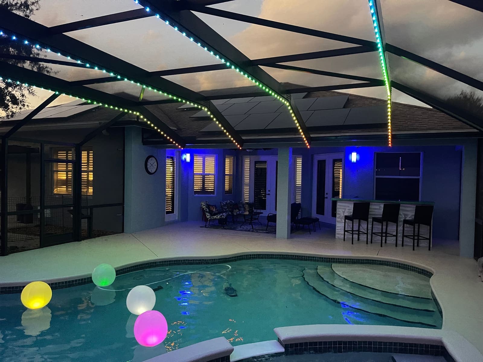 A pool cage lit for an evening gathering, water glowing below.